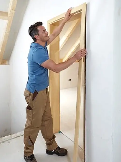 Muž montuje dřevěný zárubník interiérových dveří do stěny.