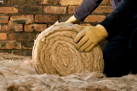 Ruka drží válcovaný minerální vatu pro zateplování domu.