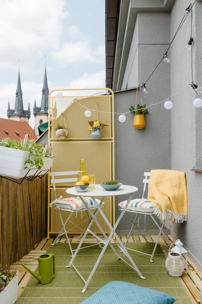 Zelená terasa s židlíčkem, stolkem a květinami u domu.