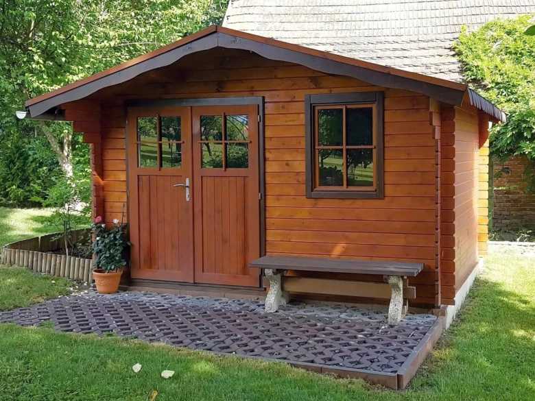 Dřevěný zahradní domek s lavičkou a květináčem na trávníku.