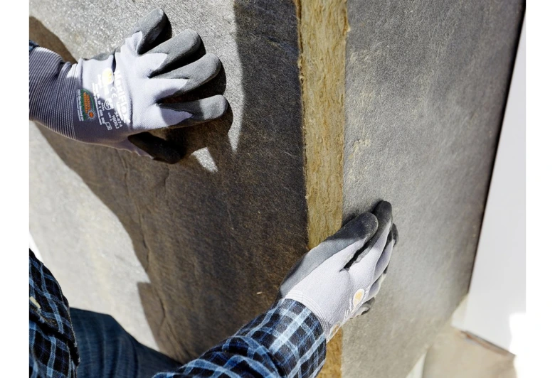 Ruční instalace tepelné izolace na stěnu během stavby.