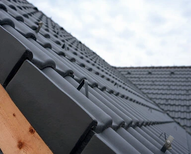 Instalace šindelových střech s tmavými taškami na dřevěném nosníku.