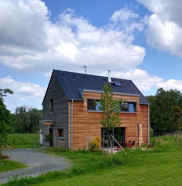 Modern dřevostavba s solárními panely na pozadí zelené krajiny.