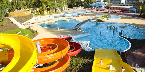 Venkovní akvapark s barevnými skluzavkami a bazény pro návštěvníky.