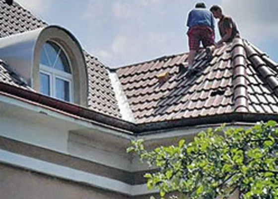 Dva muži opravují střechu domu s taškami.