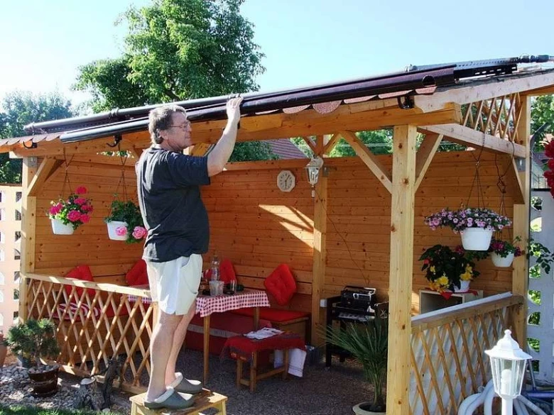 Muž montuje plastový okap na dřevěnou zahradní pergolu.