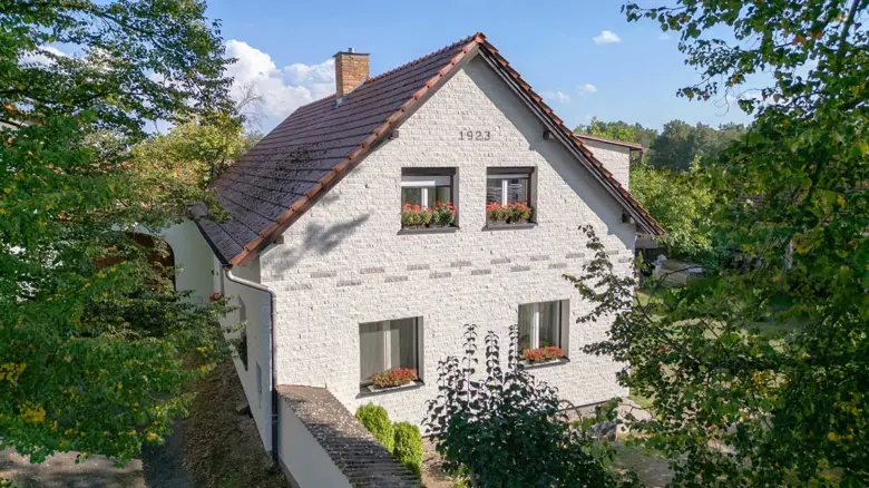 Bílá fasáda rodinného domu s květinami v oknech