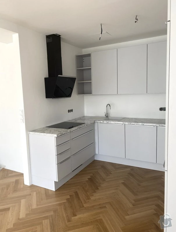 Moderní kuchyň po rekonstrukci s bílými skříněmi a dřevěnou podlahou.