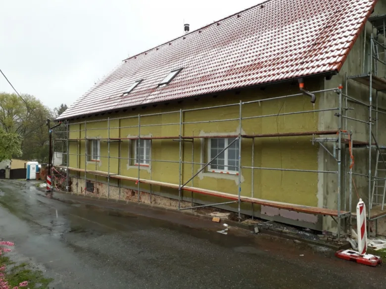 Dům s izolačními deskami na fasádě pod šedým nebem.