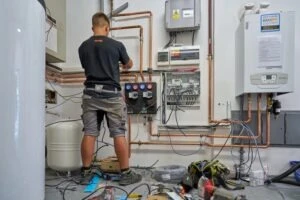 Technik montuje plynový kotel s měděnými potrubími v nehotové místnosti.