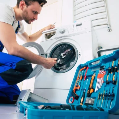 Technik opravuje bílou pračku s otevřenou dvířky.