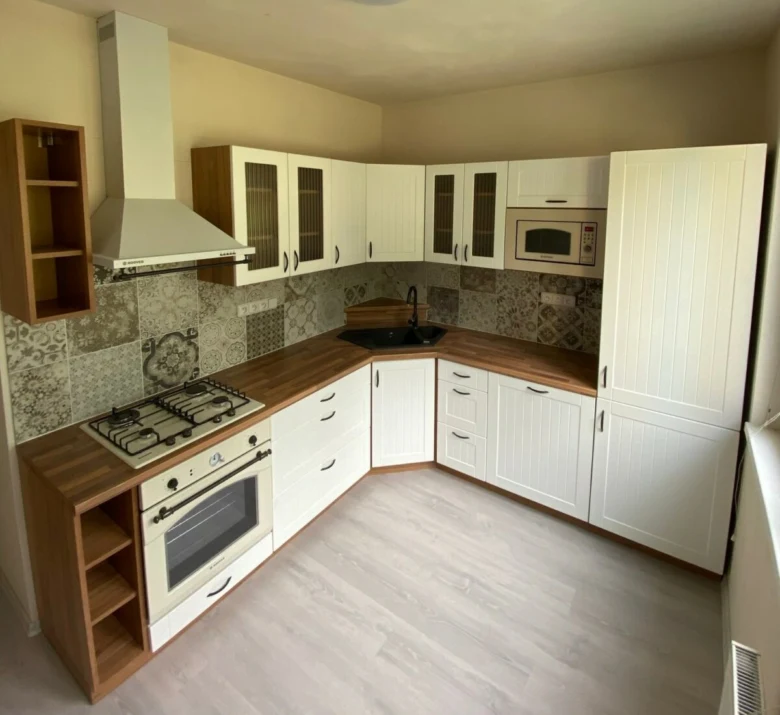Přestavěná kuchyňská linka s bílými skříni a dřevovrstvenou pracovní deskou.