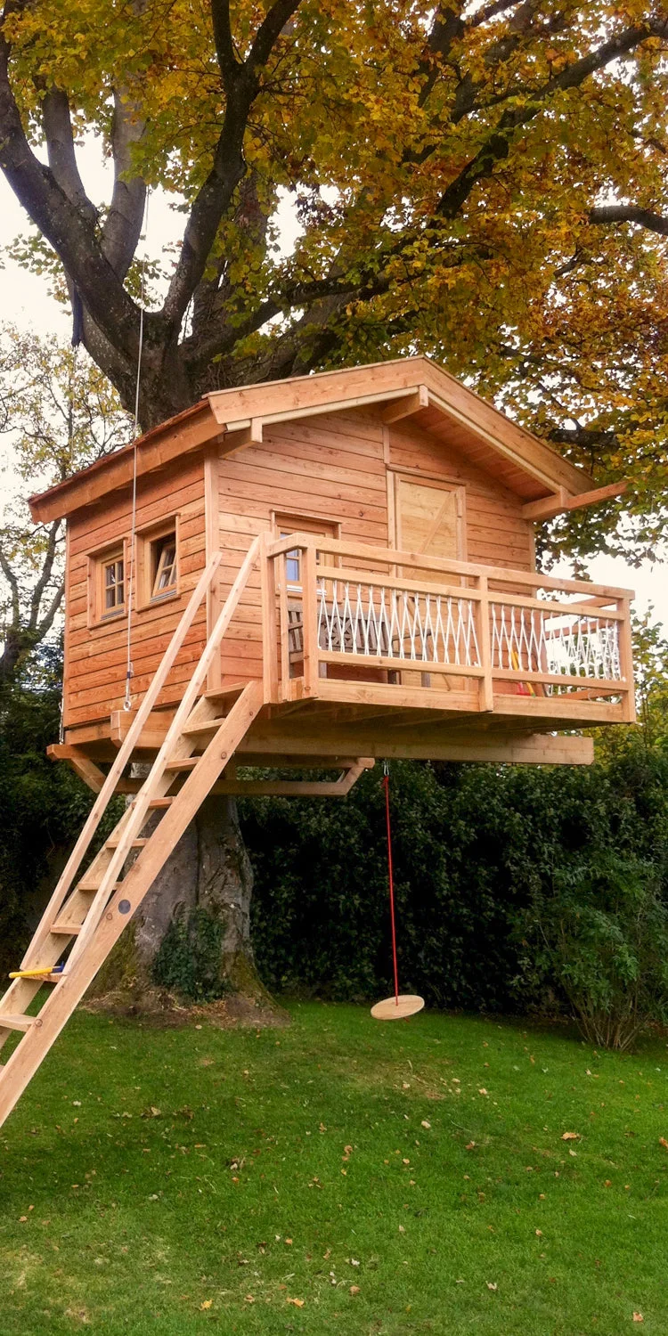 Dřevěný domek na stromě s balkonem a houpačkou.
