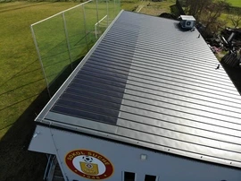Fotovoltaické panely na střeše budovy vedle zelené trávy.