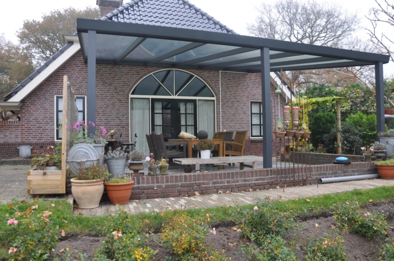 Moderní pergola s skleněnou střechou na terase u cihlového domu.