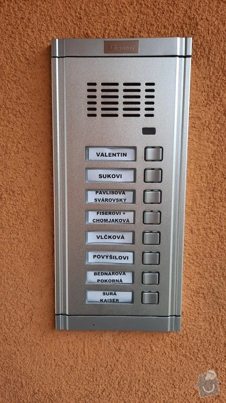 Stříbrný bytový zvonkový systém s tlačítky pro jednotlivé domácnosti.