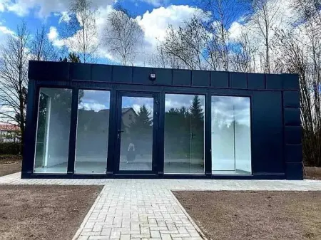 Moderní kontejnerový dům s velkými okny na pozadí stromů.